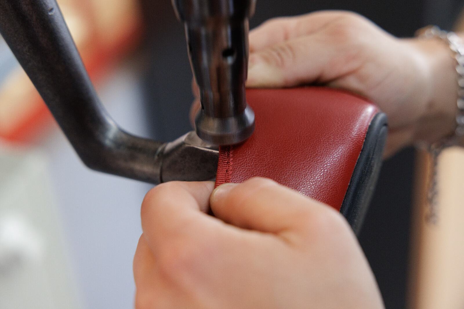 Manos de una operaria guiando el ribete de un zapato de piel roja bajo la máquina de coser.