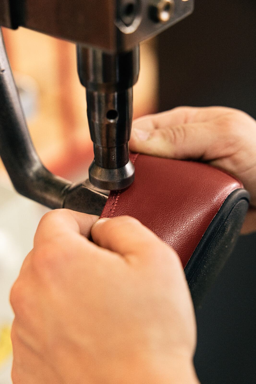 Manos guiando el ribete de un zapato de piel roja bajo una máquina de coser.